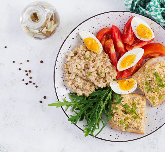 Fresh salad. Breakfast bowl with oatmeal, sandwiches with chicken rillettes, tomato and boiled egg. Healthy food. Top view, flat lay